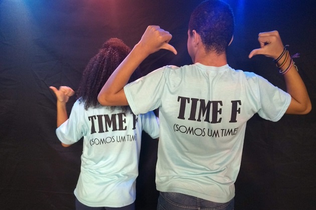 Dois alunos, um menino e uma menina, de costas, exibem o uniforme do Time F da Escola Municipal Finlândia